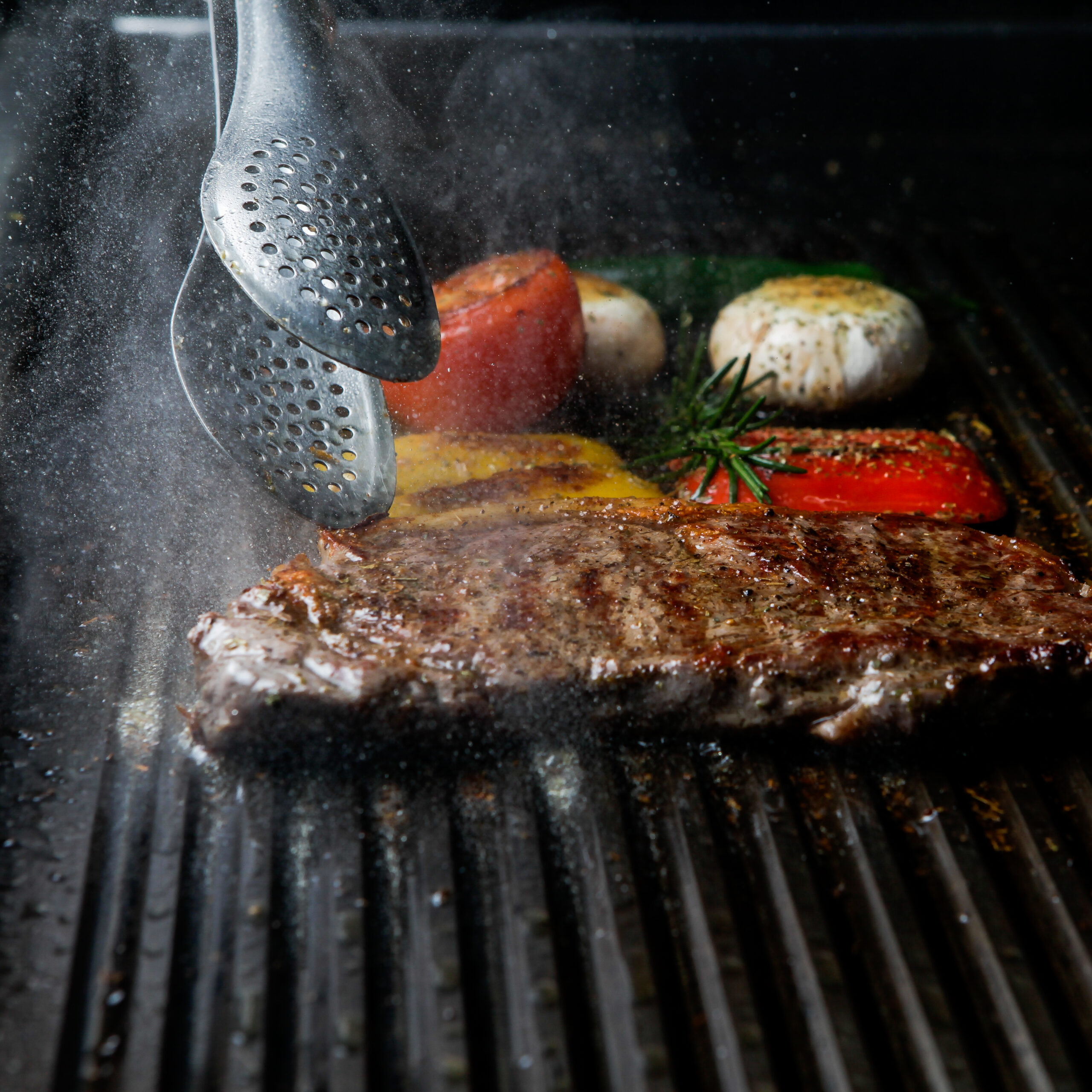 Side view grilled steak with rosemary and mushrooms and barbecue tongs in barbecue on dark background